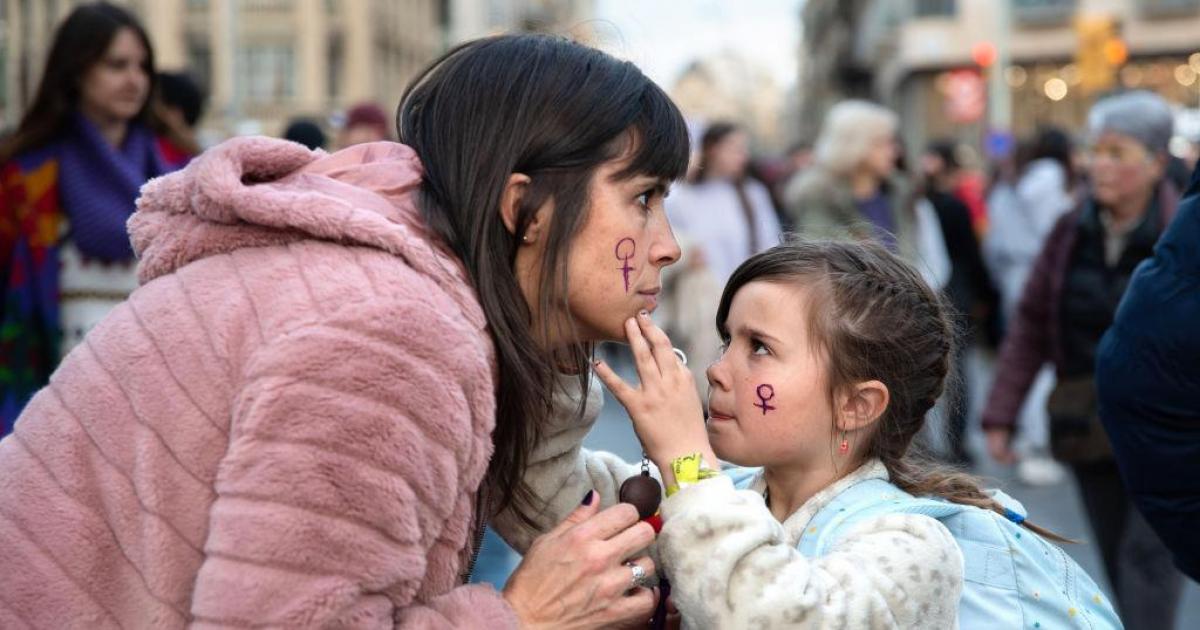 Una niña le pinta la cara a una mujer durante la manifestación del 8 de marzo de 2023 en Barcelona.