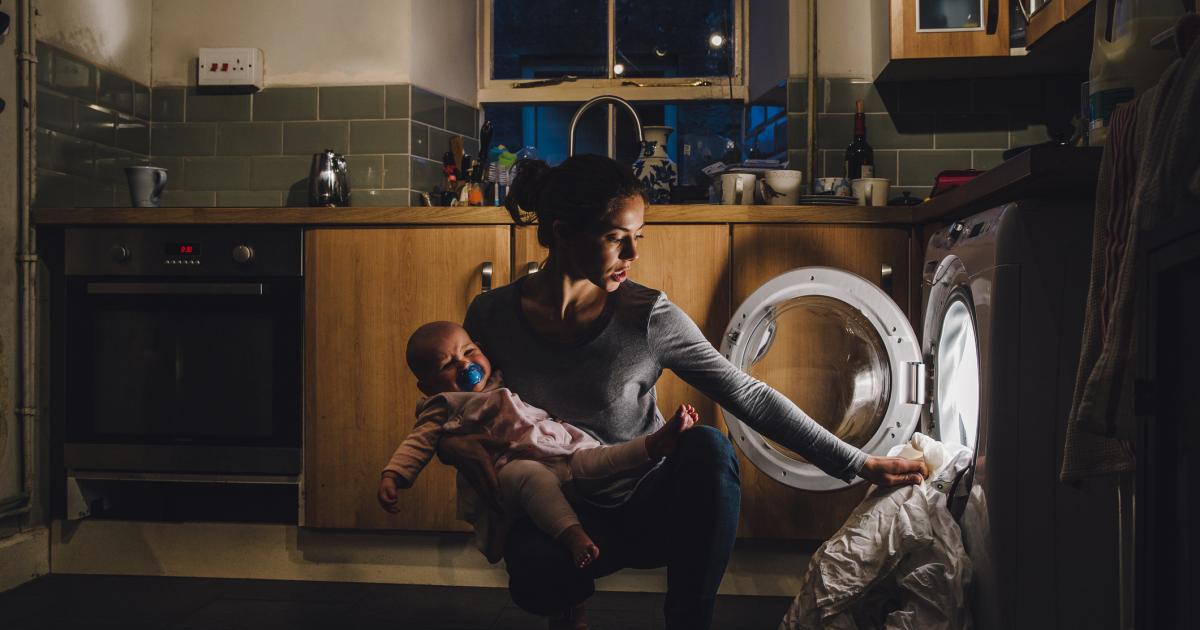 Imagen de archivo de una madre poniendo la lavadora mientras sostiene a su bebé.