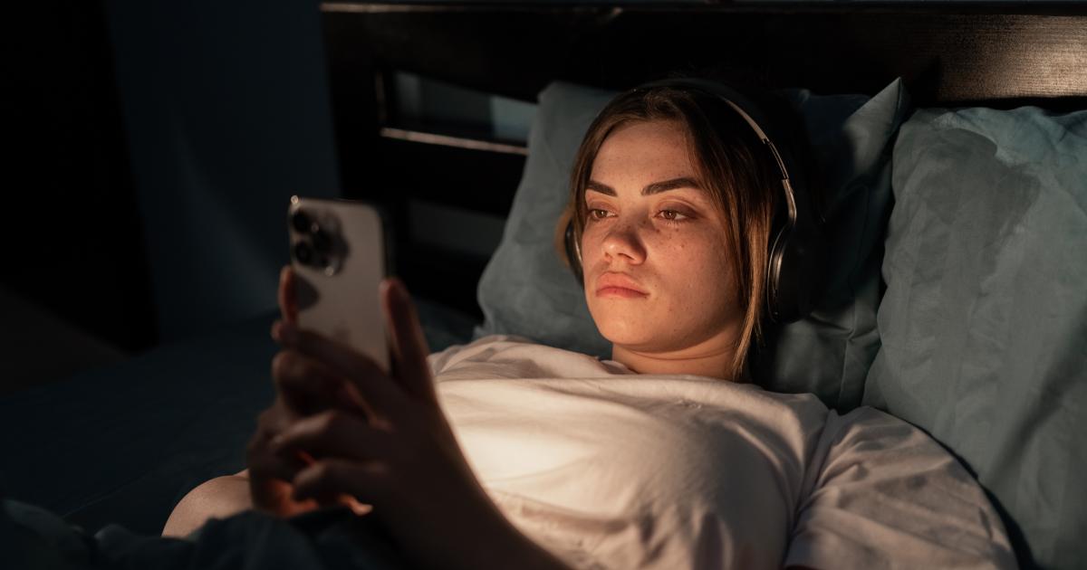 Imagen de archivo de una mujer joven en la cama con un móvil.