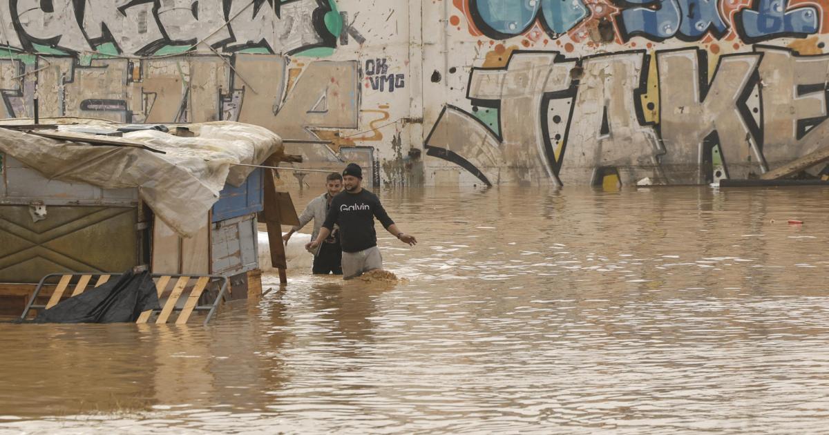 Dos personas vadean un terreno de chabolas inundado junto a la V-30 a causa de las lluvias torrenciales de las últimas horas.