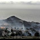 Varias casas rodeadas de humo y con un pequeño foco aún encendido, en La Gomera.