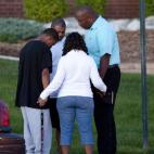 A small group prays outside Gateway High School where witness were brought for questioning Friday, July 20, 2012 in Aurora, Colo. A gunman wearing a gas mask set off an unknown gas and fired into the crowded movie theater killing 12 people and ...