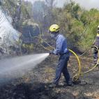 Dos bomberos rocían con agua la vegetación quemada, en los alrededores de La Jonquera.