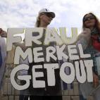 Una manifestante sujeta una pancarta en la que se puede leer 'Frau Merkel Lárgate' durante una protesta frente la sede parlamentaria griega, en Atenas.