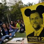 Un grupo de manifestantes esperan el inicio de la protesta, al lado un anuncio de la marcha con la imagen de Mariano Rajoy. 