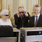 La reina Isabel II de Inglaterra y el productor John McAndrew (en el centro de la imagen) luciendo gafas 3D, junto al director de cine John Bennett (derecha), en el palacio de Buckingham en Londres, Reino Unido, durante la grabación del mensaje...
