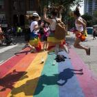 Tres mujeres saltan sobre un arcoíris pintado en el suelo en una calle de Toronto.