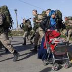 La refugiada siria Hadra Annasan empuja el carrito de su hijo Barakat en Melilla mientras varios soldados marchan para realizar unos ejercicios.