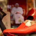 Un detalle de uno de los zapatos rojos del papa Benedicto XVI con una foto del pontífice al fondo de la tienda.