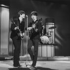 Bassist Paul McCartney and guitarist George Harrison (1943 - 2001) sing at a microphone as the Beatles perform at the London Palladium. Drummer Ringo Starr plays from a riser in the background. London, England, January 1964. (Photo by Leslie Lee...