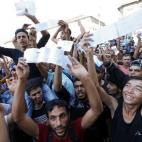Jóvenes migrantes ondean sus billetes de tren ante los medios.