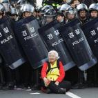 Una mujer permanece sentada frente a los antidisturbios que bloquean la carretera para proteger a los manifestantes en una protesta contra el Gobierno el 24 de abril de 2015 en Seúl. Los sindicatos convocaron una huelga general contra las polí...