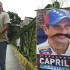 A man walks by a political propaganda poster with a picture of Venezuelan opposition presidential candidate Henrique Capriles with a painted mustache, along a street at Petare slum in Caracas on April 13, 2013. Venezuela's government mobilized ...