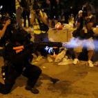 Un agente antidisturbios lanza botes de humo a los manifestantes, a las puertas del Parlamento.