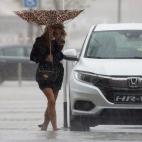 Una mujer sujeta el paraguas intentando que no se le vuele debido al viento y a la lluvia en Málaga.