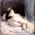 Una mujer desnuda recostada de lado en una cama. Daguerrotipo estereoscópico coloreado a mano. 1850.