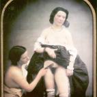 Una mujer semidesnuda peina el vello púbico de otra con la falda levantada y la blusa bajada. Daguerrotipo estereoscópico coloreado a mano. 1850.