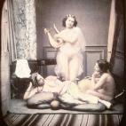Tres mujeres semidesnudas en un estudio recreando escenas similares a un harén y a la antigua Grecia. La mujer del centro sujeta una lira y lleva un velo transparente. Daguerrotipo estereoscópico coloreado a mano. 1850.