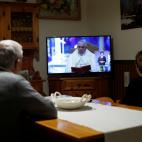 Un par de feligreses atienden a las palabras del papa por televisi&oacute;n