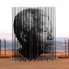 El artista Marco Cianfanelli ideó con el rostro de Mandela para rememorar el 50 aniversario de su apresamiento. Las 50 columnas, de entre 6,5 y 9 metros de alto, aparentemente desordenadas, si se miran desde una dirección concreta, conforman l...