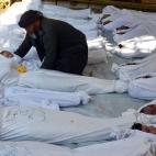 Un hombre levanta el cuerpo de un niño muerto entre los cadáveres de las personas asesinadas con gas sarín en la región de Ghouta, Siria, el 21 de agosto de 2013. Activistas sirios denunciaron que al menos 213 personas, entre ellas mujeres y...