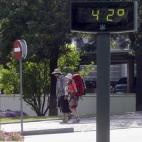 Unos turistas pasan junto a un termómetro por el centro de Córdoba que se encuentra en alerta amarilla por altas temperaturas.