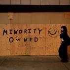 A woman walks past a store boarded up with a message as protests over the death of George Floyd continue Sunday, May 31, 2020, in Los Angeles. Armed National Guard soldiers lined the steps of Los Angeles City Hall, and cities across California d...