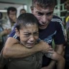Dos varones lloran la muerte de un familiar, muerto en la operación israelí contra el centro de la ONU.