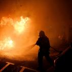 A firefighter tries to put off a fire on the street during clashes between protestors and police in Barcelona, Spain, Wednesday, Oct. 16, 2019. Spain's government said Wednesday it would do whatever it takes to stamp out violence in Catalonia, w...