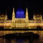 Un barco turístico navega por el Danubio frente al Parlamento húngaro, iluminado por el Día del Autismo.