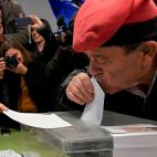 Un hombre que luce una típica berretina catalana en la cabeza besa su papeleta justo antes de depositarla en la urna.