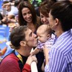 Phelps da un beso a su hijo Boomer, en brazos de su pareja y madre del niño, Nicole Johnson. La madre del nadador, en el centro, observa la escena emocionada después de que Phelps ganara la prueba masculina de 200 metros mariposa en los Juegos...