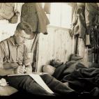 Fotografía tomada en el campamento Randalstown en el Condado de Antrim en 1915. John Ewing, de Belfast y amigo de Hackney, escribe su diario o una carta a su familia mientras sus compañeros duermen. Ewing alcanzó posteriormente el rango de sa...