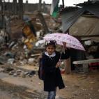 Una estudiante gazatí sostiene un paraguas mientras camina por las ruinas de lo que eran casas, supuestamente destruidas en un bombardeo israelí.
