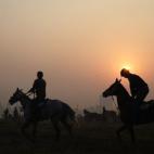 Dos jinetes indios montan a caballo durante una sesión de práctica en el Royal Calcutta Turf Club una mañana nublada.