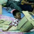 Un niño juega con una caja de cartón mientras está refugiado en un pabellón de baloncesto reconvertido en centro de evacuación en Quezon, al este de Manila (Filipinas), por el paso del tifón Hagupit, que ha dejado al menos 27 muertos y 1,6...