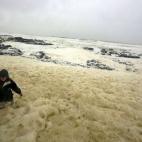Un hombre camina entre la espuma del mar provocada por las tormentas en la ciudad de Portstewart (Irlanda del Norte).