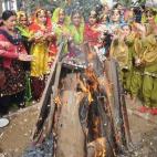 Un buen número de estudiantes ataviadas con coloridos trajes se reúne en torno a un fuego durante la celebración del festival Lohri en India. Esta fiesta marca la culminación del invierno.