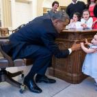 President Barack Obama holds the hand of Lincoln Rose Pierce Smith, the daughter of former Deputy Press Secretary Jamie Smith, in the Oval Office, April 4, 2014. Watching from the other side of the Resolute Desk are Elsa Smith, age 5, and Sage S...