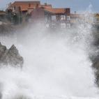 Una ola rompe junto a las casas de Liencres, en Cantabria, cuya comunidad se encuentra en alerta por fuertes vientos y fenómenos costeros.