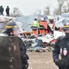 Policemen stand next to agents dismantling shacks as two migrants stand on a shelter's roof on March 1, 2016 in the 'Jungle' migrant camp in the French northern port city of Calais. Workers were due to start a second day of destruction in the so...