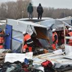 Agents dismantle shacks as two migrants stand on a shelter's roof on March 1, 2016 in the 'Jungle' migrant camp in the French northern port city of Calais. Workers were due to start a second day of destruction in the southern half of the camp, w...