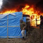 Migrants run past burning tents in a makeshift camp near Calais, France, Monday Feb. 29, 2016. Under the eye of hundreds of riot police, workers began pulling down tents and makeshift shelters in the sprawling camp in Calais on Monday, dismantli...
