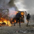 Migrants run past burning tents in a makeshift camp near Calais, France, Monday Feb. 29, 2016. French authorities have begun dismantling part of the sprawling camp locally referred to as "the jungle" where thousands are hanging out, hoping to ma...