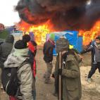 Migrants and activists watch burning makeshift shelters set on fire in the camp near Calais, northern France, Monday, Feb. 29, 2016. Under the eye of hundreds of riot police, workers began pulling down tents and makeshift shelters in the sprawli...