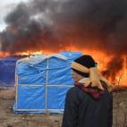 A migrant stands in front of shacks burning during the dismantling of half of the 'Jungle' migrant camp in the French northern port city of Calais, on February 29, 2016. Clashes broke out between French riot police and migrants on February 29 as...