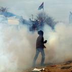 CALAIS, FRANCE - FEBRUARY 29: A migrant runs through teargas as police officers clear part of the 'jungle' migrant camp on February 29, 2016 in Calais, France The French authorities have begun dismantling part of the migrant encampment in the ...