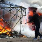 CALAIS, FRANCE - FEBRUARY 29: A migrant attempts to extinguish a fire in a burning hut as police officers clear part of the 'jungle' migrant camp on February 29, 2016 in Calais, France The French authorities have begun dismantling part of the ...