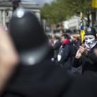 Un manifestante con careta de anonimous y casco de policía hace fotos en la protesta por el Primero de Mayo de Londres, en Trafalgar Square.