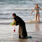 Una mujer musulmana que lleva un Hijab se coloca en las aguas en el mar Mediterráneo mientras que un israelí se coloca cerca en la playa en Tel Aviv Una mujer musulmana lleva con Hijab se baña en el mar Mediterráneo mientras una chica israel...